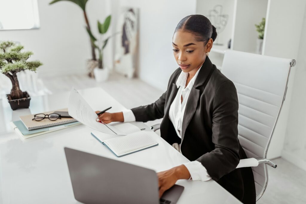 Professional recruitment concept. Black female HR manager using laptop, holding candidate's CV